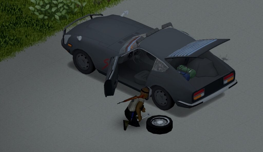 A grey sports car with its boot and front door open. A person kneels beside it changing a tyre.